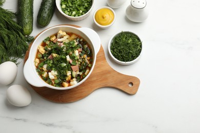 Photo of Delicious okroshka soup and ingredients on white table, flat lay. Space for text