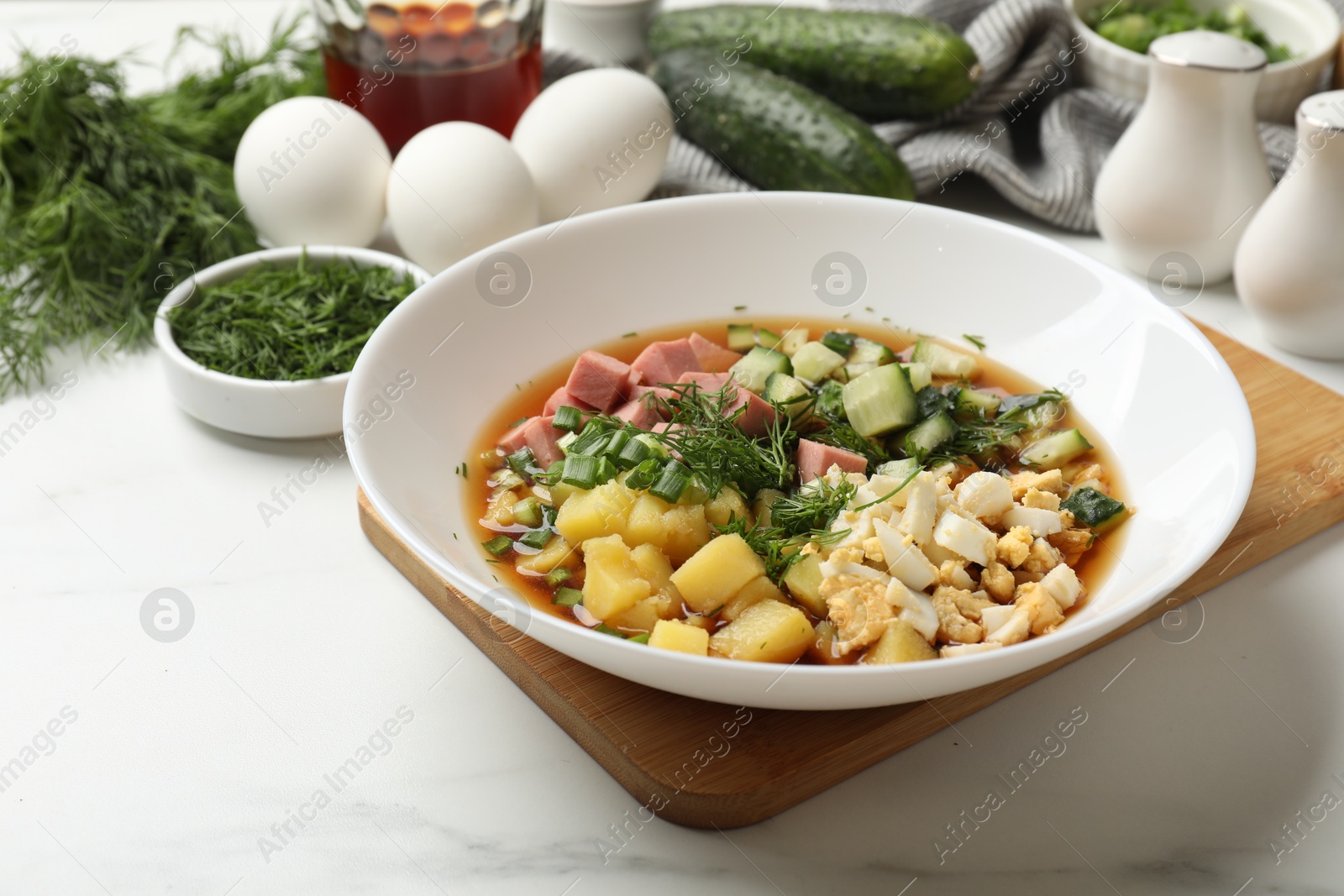 Photo of Delicious okroshka soup and ingredients on white table, closeup