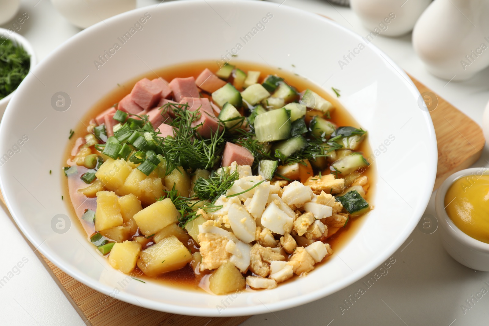 Photo of Delicious okroshka soup and ingredients on white table, closeup