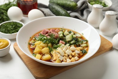 Photo of Delicious okroshka soup and ingredients on white table, closeup