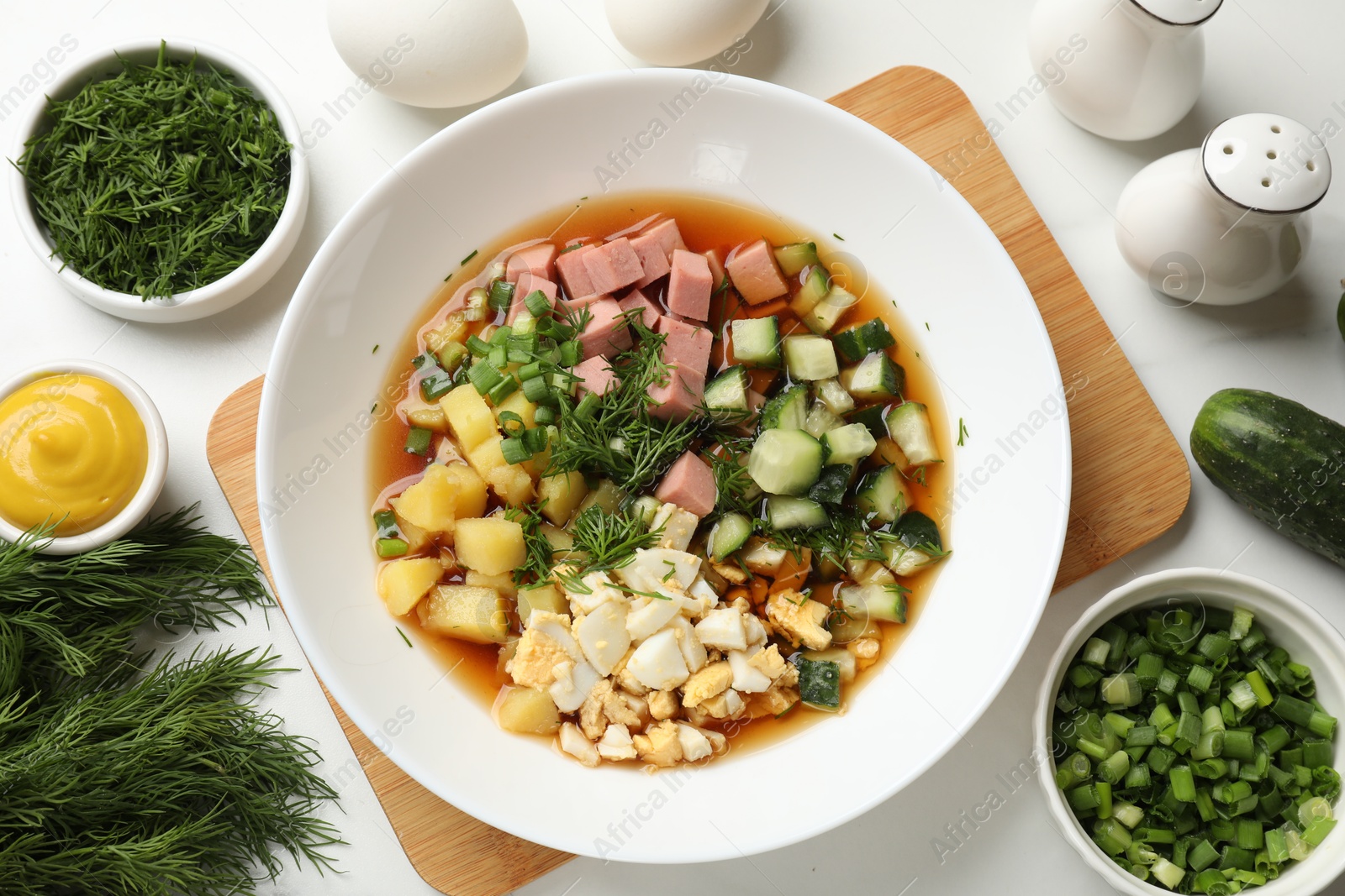 Photo of Delicious okroshka soup and ingredients on white table, flat lay