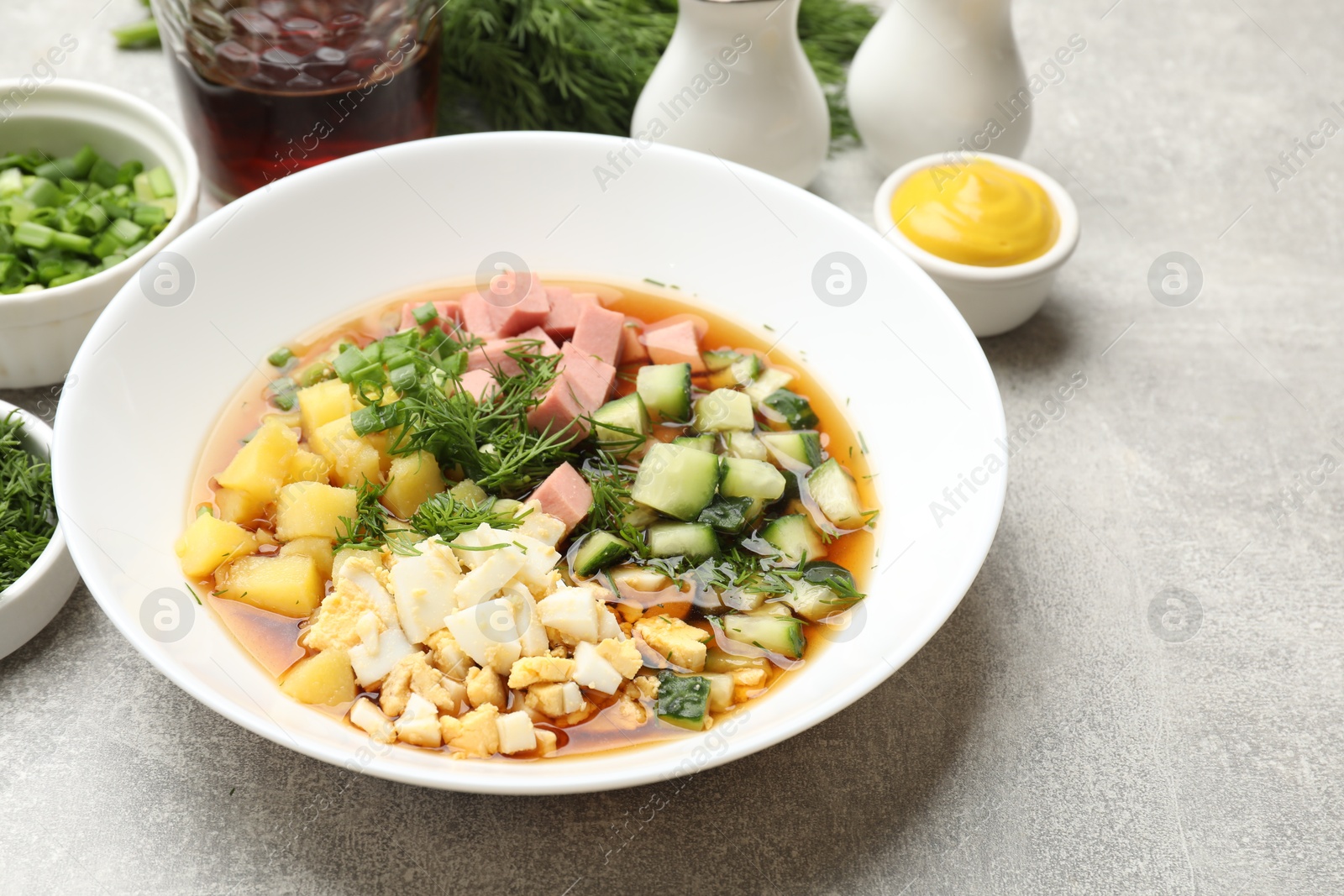 Photo of Delicious okroshka soup and ingredients on grey table, closeup