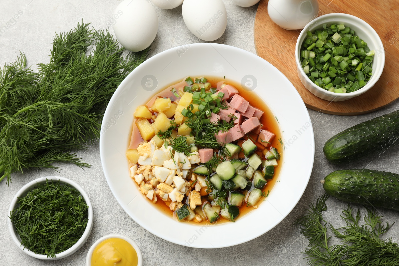 Photo of Delicious okroshka soup and ingredients on grey table, flat lay