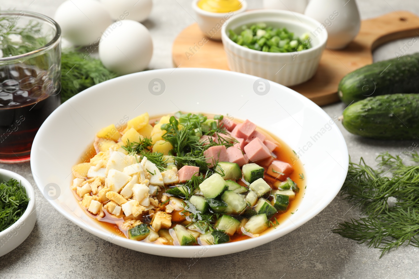 Photo of Delicious okroshka soup and ingredients on grey table, closeup