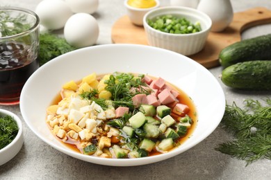 Photo of Delicious okroshka soup and ingredients on grey table, closeup