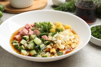 Photo of Delicious okroshka soup and ingredients on grey table, closeup