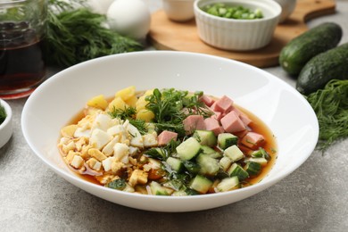 Photo of Delicious okroshka soup and ingredients on grey table, closeup