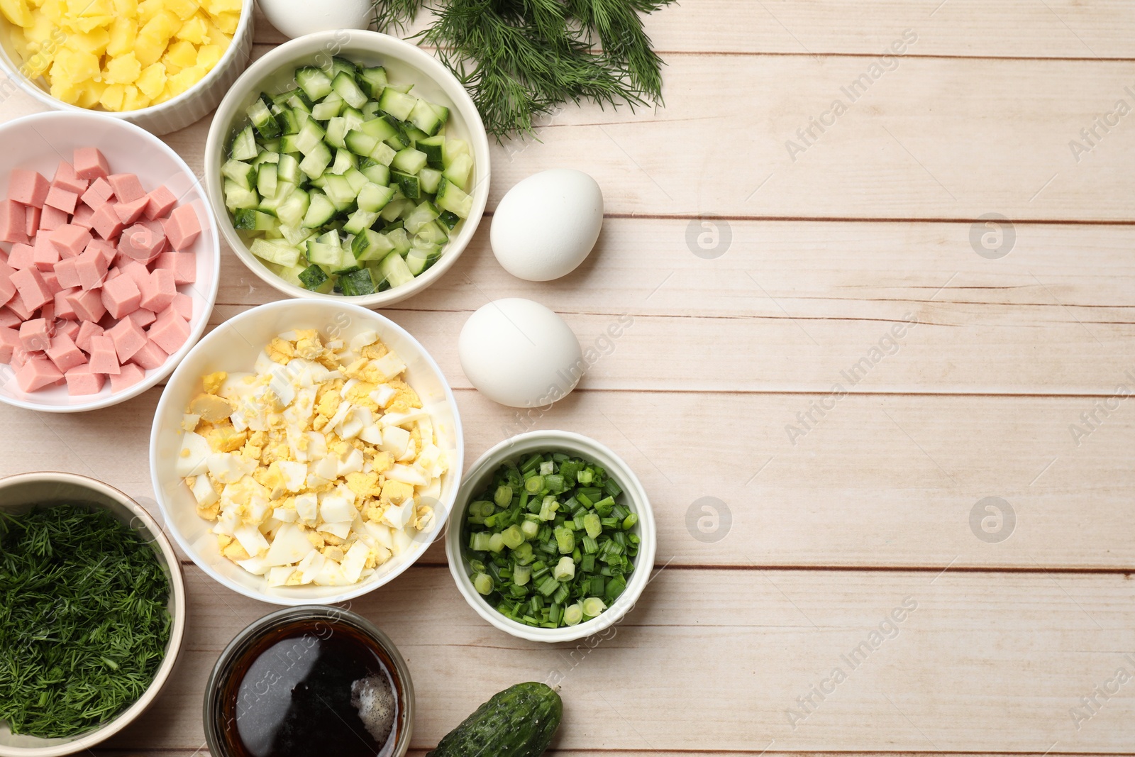 Photo of Different ingredients for okroshka soup on white wooden table, flat lay. Space for text