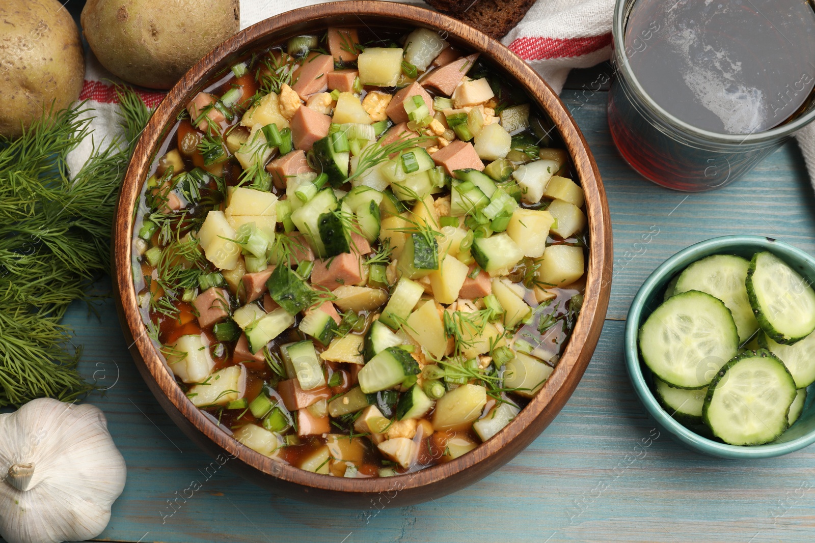 Photo of Delicious okroshka soup with kvass and ingredients on blue wooden table, flat lay