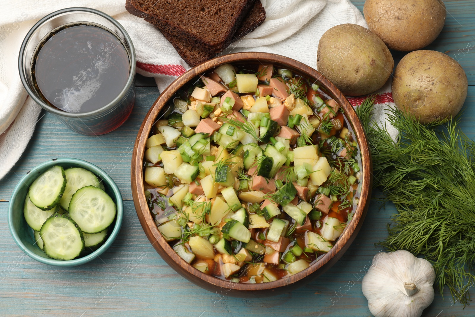 Photo of Delicious okroshka soup with kvass and ingredients on blue wooden table, flat lay