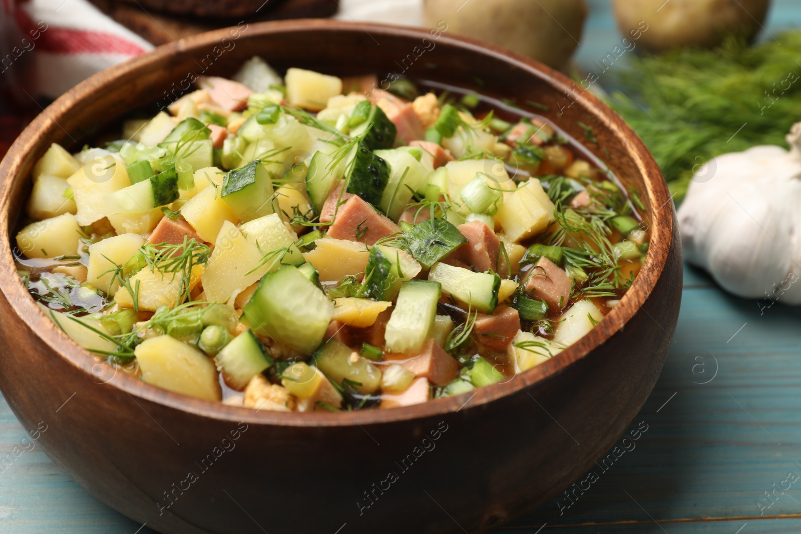 Photo of Delicious okroshka soup with kvass and ingredients on blue wooden table, closeup