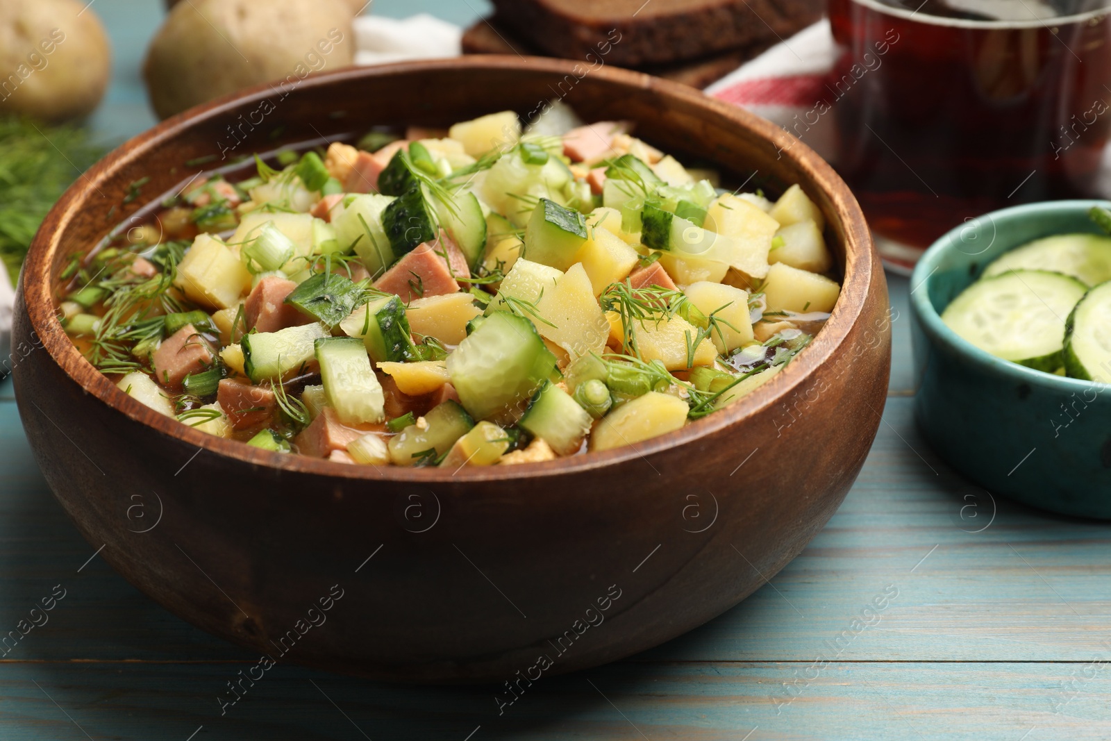 Photo of Delicious okroshka soup with kvass and ingredients on blue wooden table, closeup