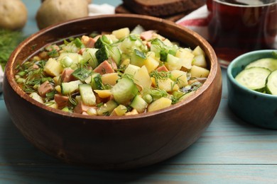 Photo of Delicious okroshka soup with kvass and ingredients on blue wooden table, closeup