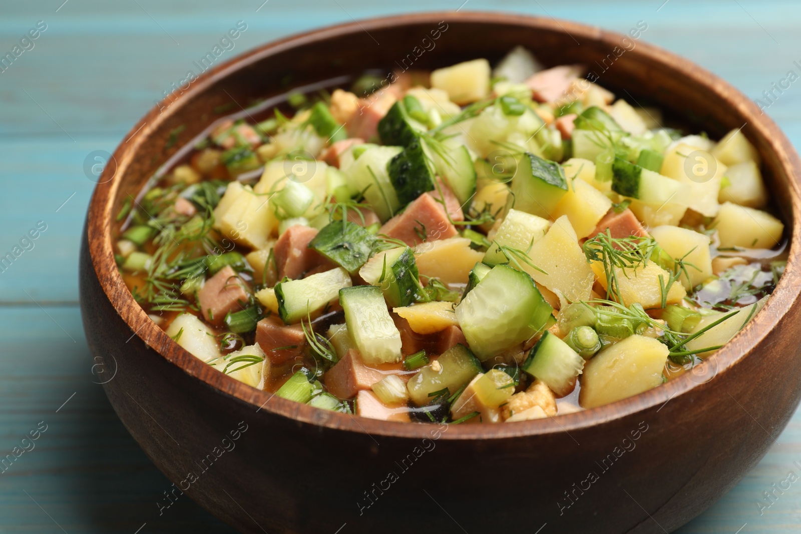 Photo of Delicious okroshka soup with kvass on blue wooden table, closeup