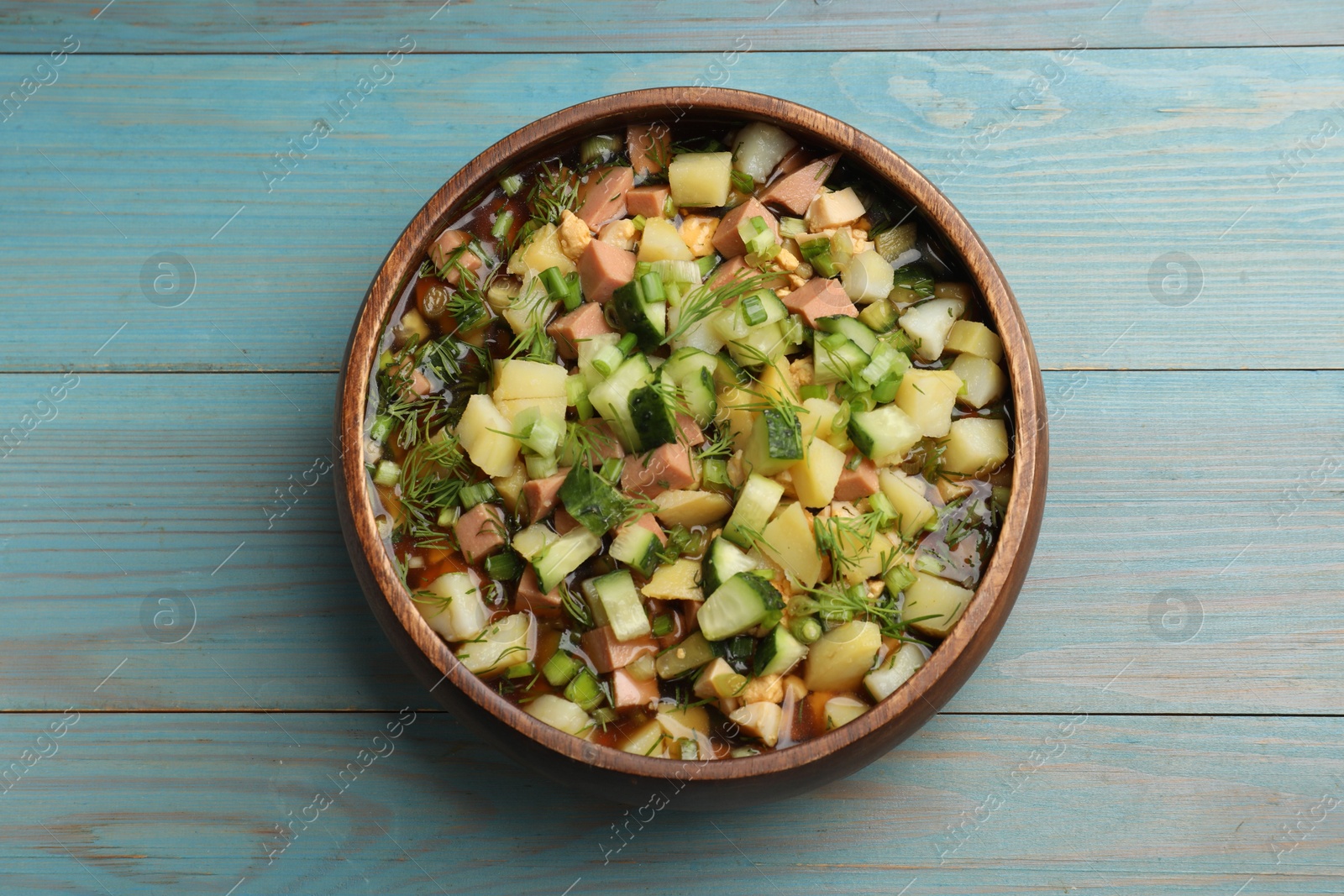 Photo of Delicious okroshka soup with kvass on blue wooden table, top view