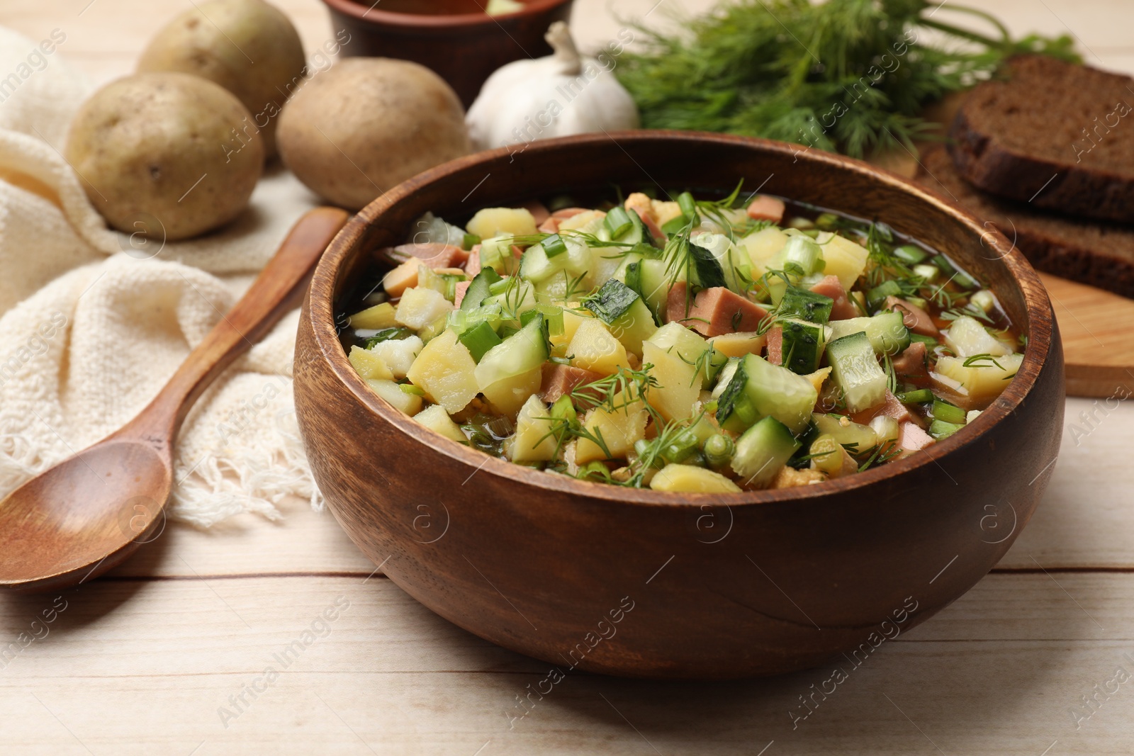 Photo of Delicious okroshka soup with kvass and ingredients on white wooden table, closeup