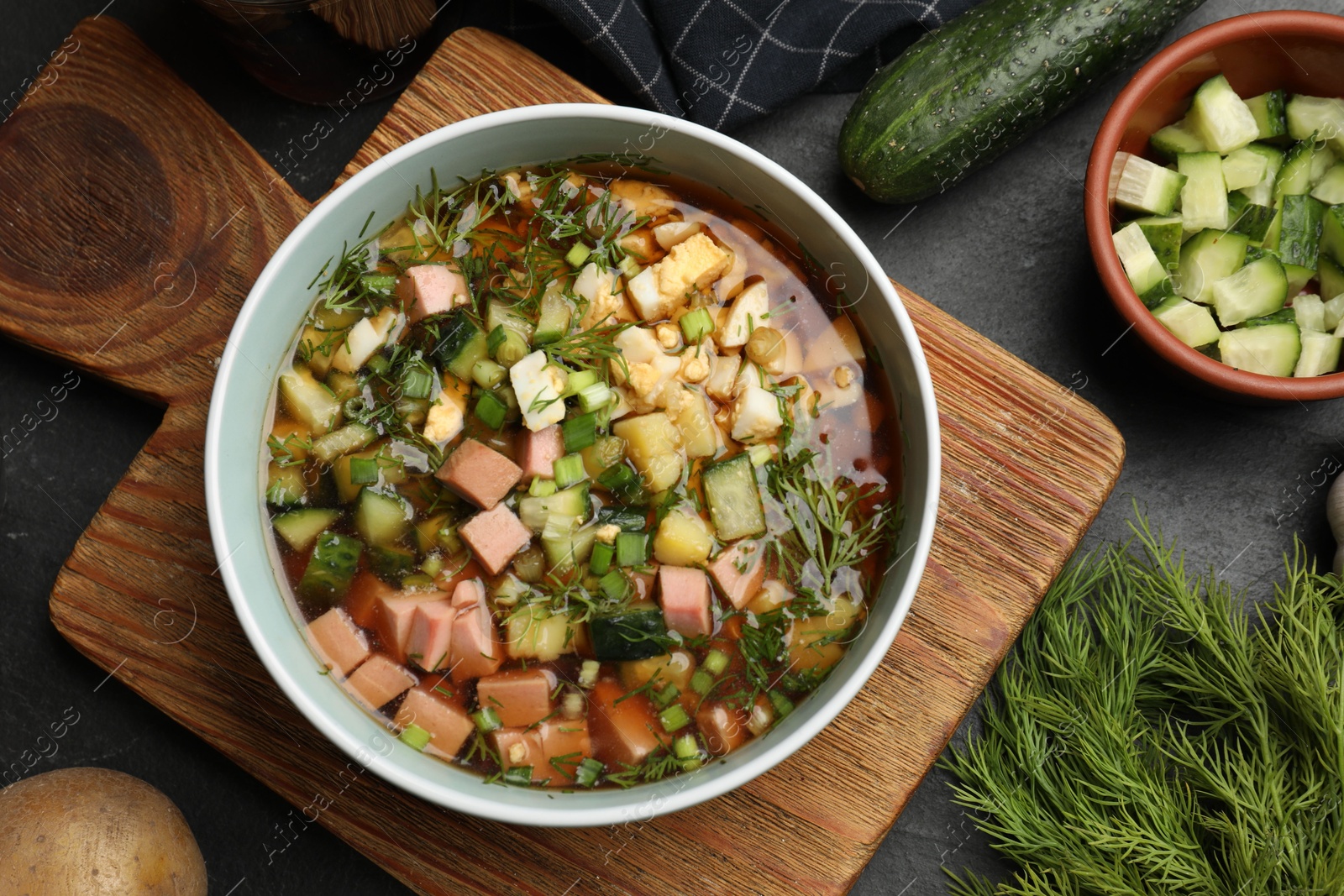 Photo of Delicious okroshka soup with kvass and ingredients on black table, flat lay