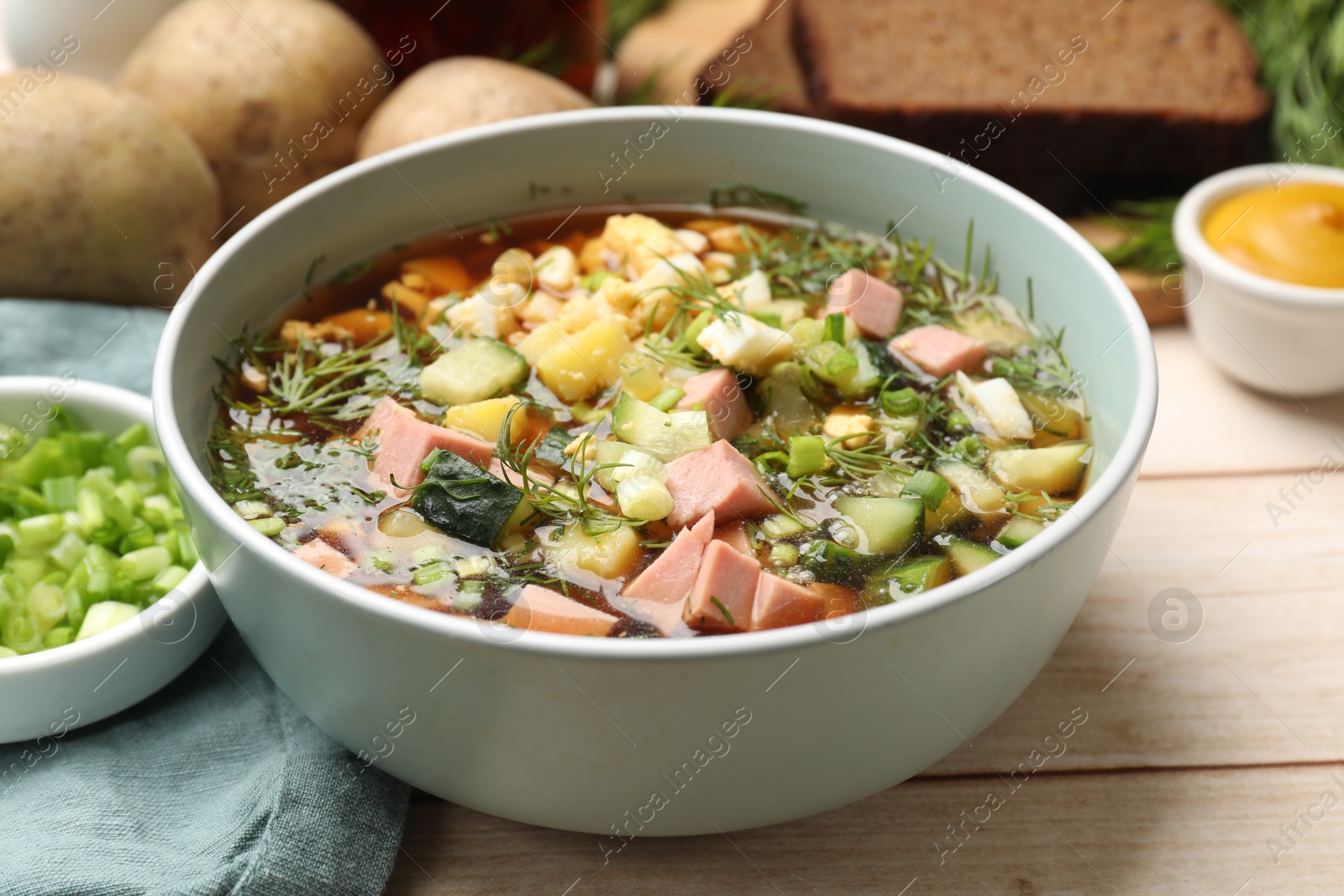 Photo of Delicious okroshka soup with kvass and ingredients on white wooden table, closeup