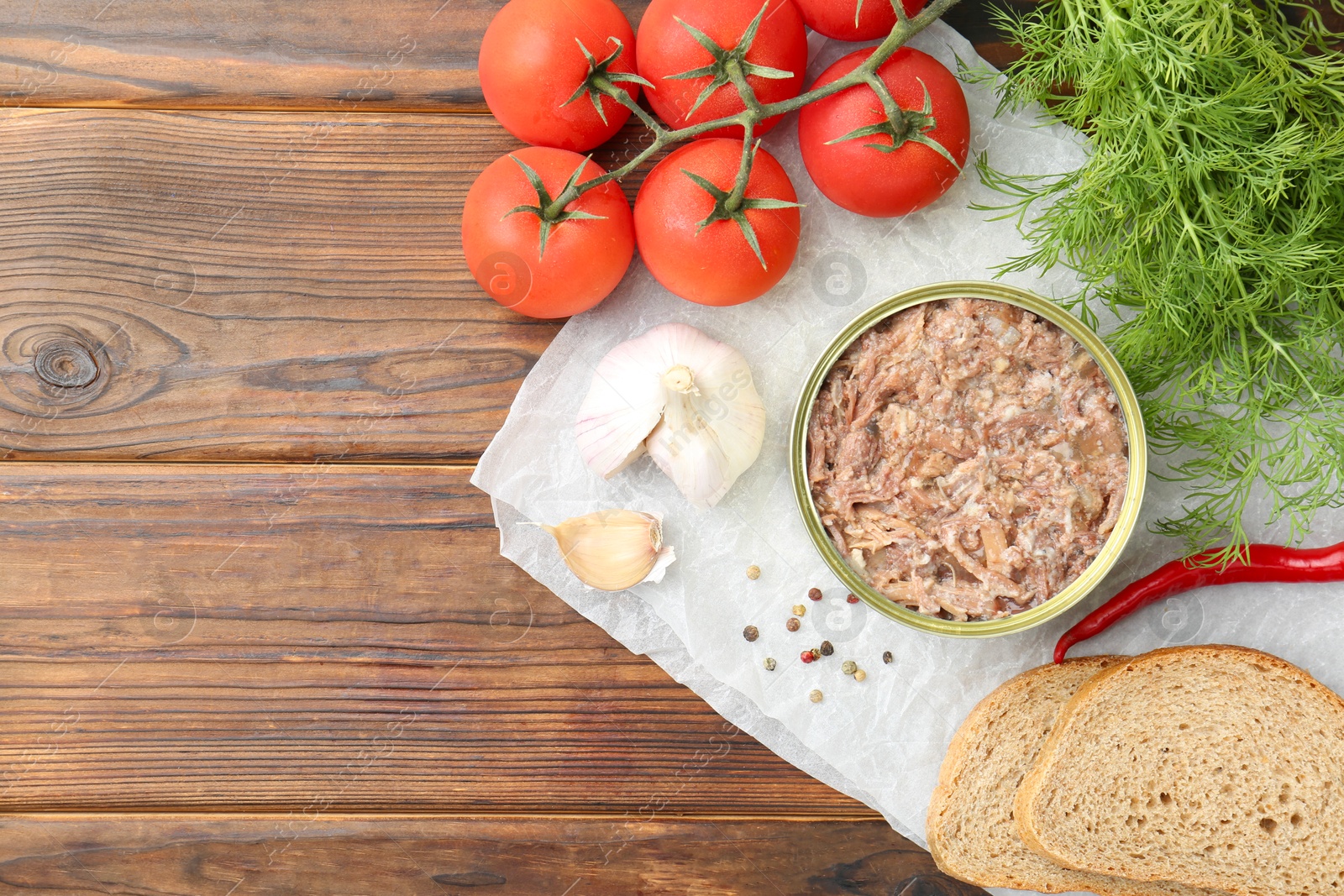 Photo of Canned meat in tin can served on wooden table, flat lay. Space for text