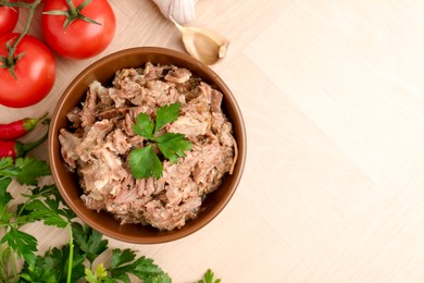 Photo of Canned meat in bowl, parsley, tomatoes and garlic on wooden table, top view. Space for text