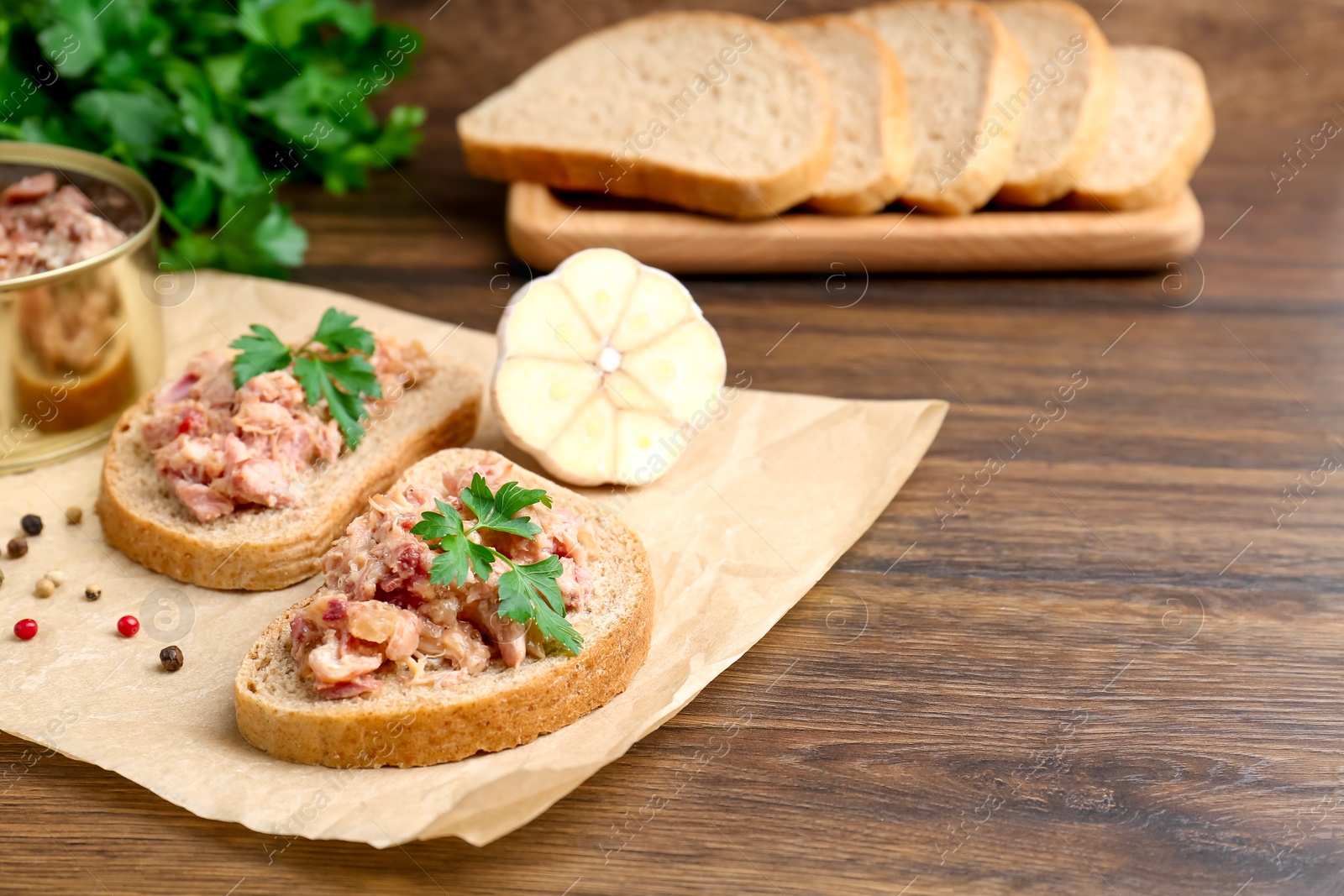 Photo of Sandwiches with canned meat, parsley, garlic and peppercorns on wooden table, closeup. Space for text