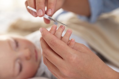 Photo of Mother cutting her cute little baby's nails on bed, closeup