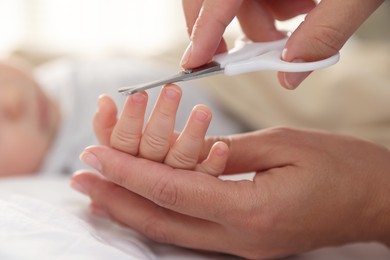 Photo of Mother cutting her cute little baby's nails on bed, closeup