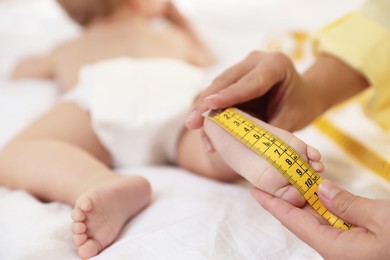 Photo of Mother measuring little baby's foot on bed, closeup