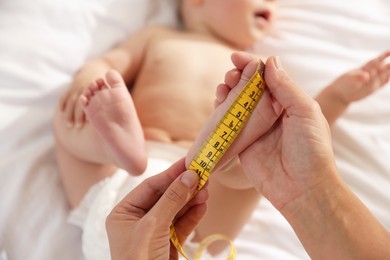 Photo of Mother measuring little baby's foot on bed, selective focus