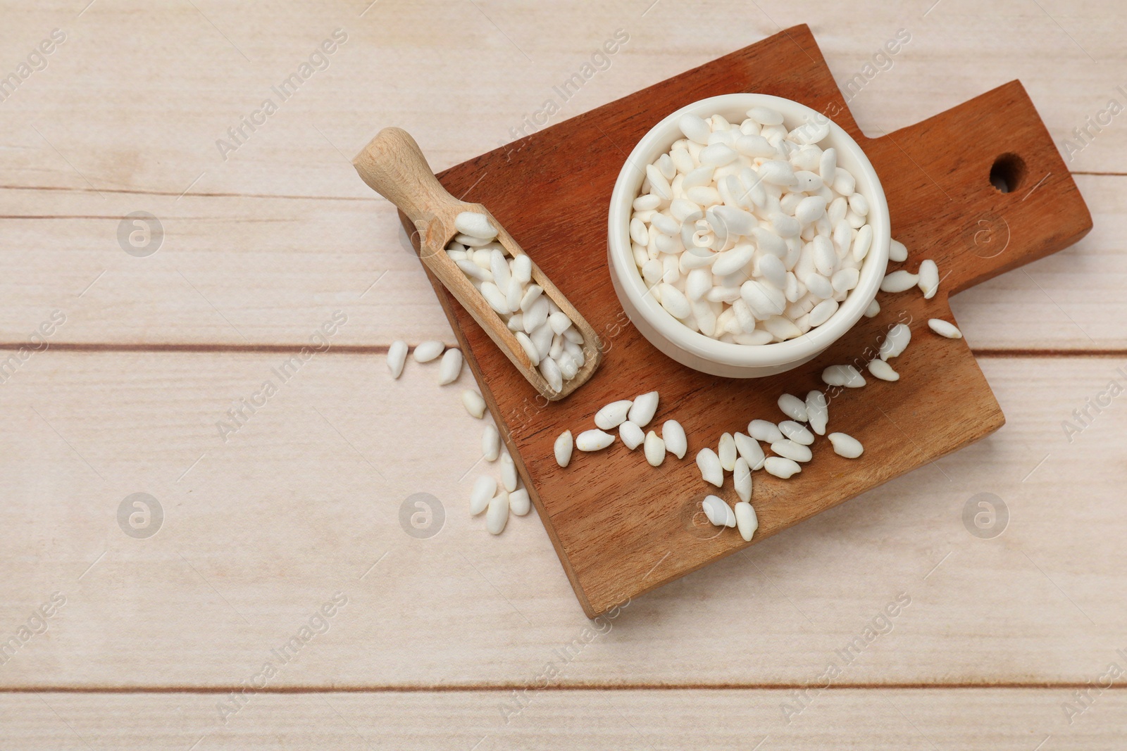 Photo of Bowl and scoop with puffed rice on white wooden table, top view. Space for text