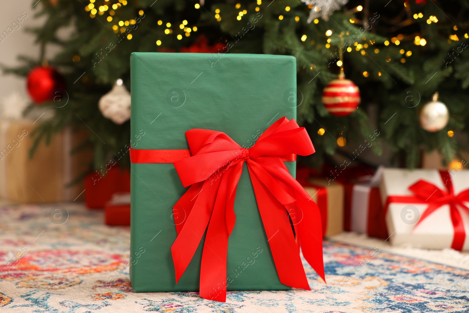 Photo of Gift box with bow near Christmas tree in room, selective focus