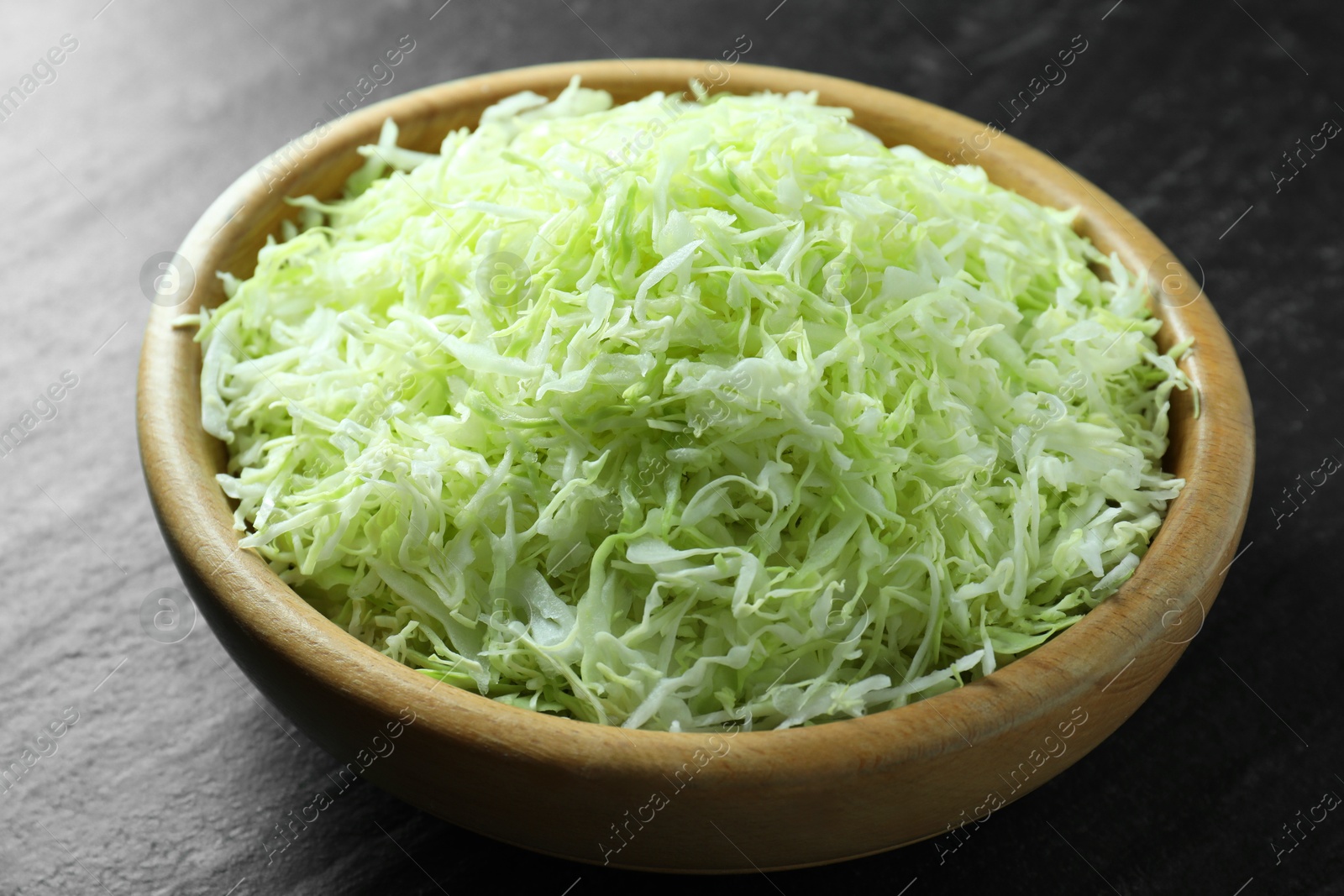 Photo of Fresh shredded cabbage on black table, closeup