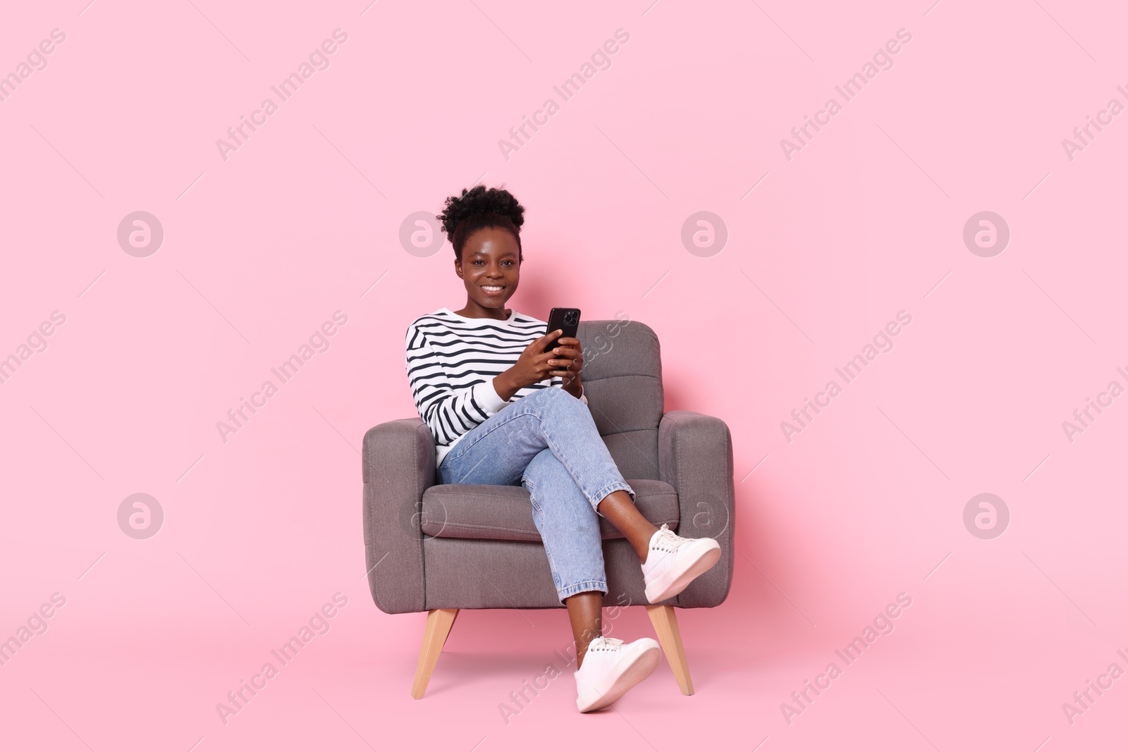 Photo of Smiling woman with smartphone sitting in armchair on pink background