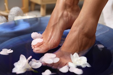 Photo of Woman soaking her feet in bowl with water and flowers on floor, closeup. Spa treatment