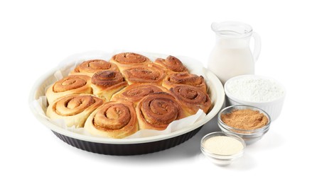 Photo of Freshly baked cinnamon rolls in baking dish and ingredients isolated on white