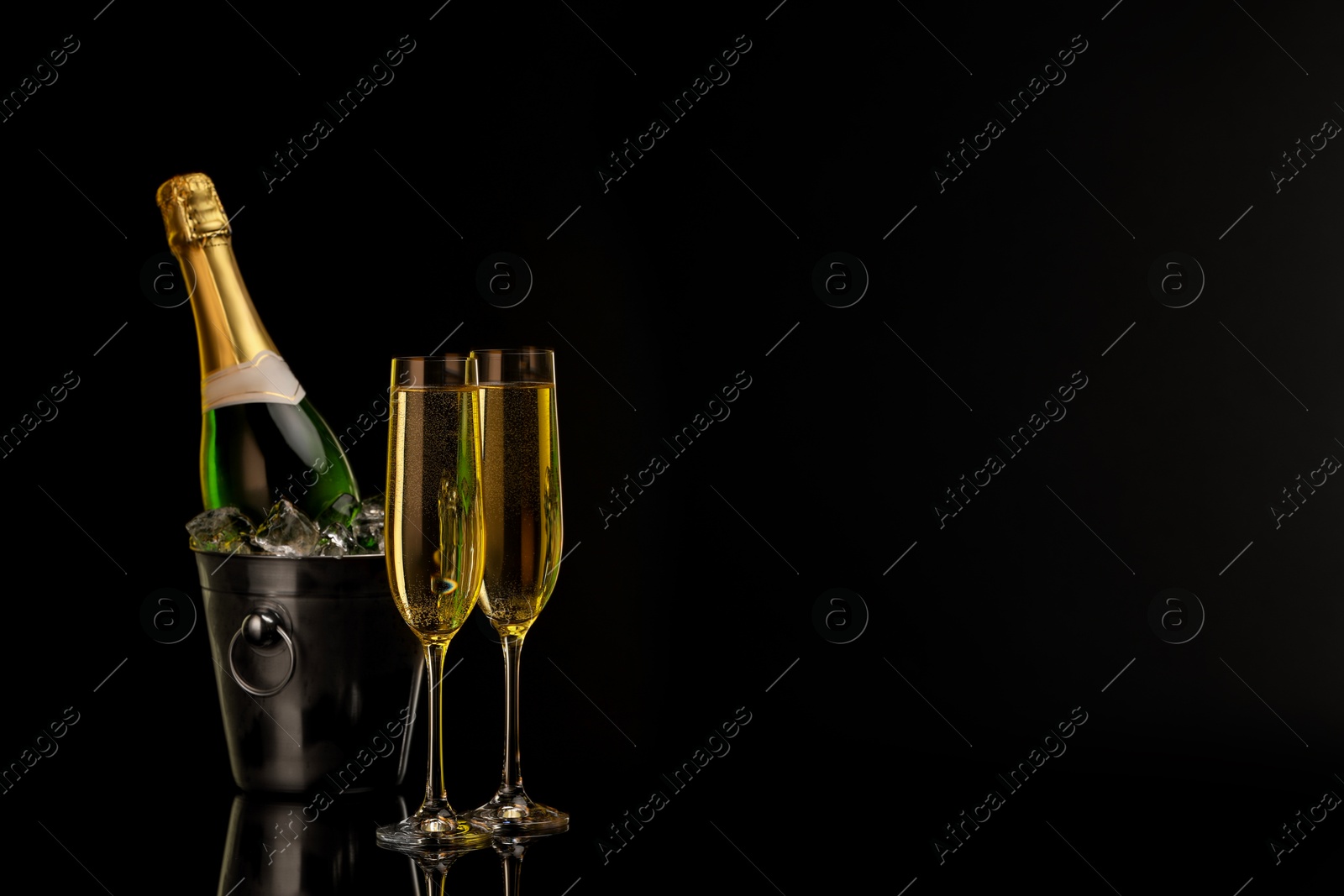 Photo of Glasses of sparkling wine and bottle in cooler bucket on black background. Space for text