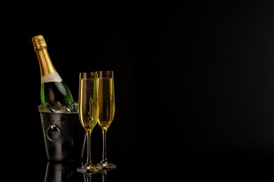 Photo of Glasses of sparkling wine and bottle in cooler bucket on black background. Space for text