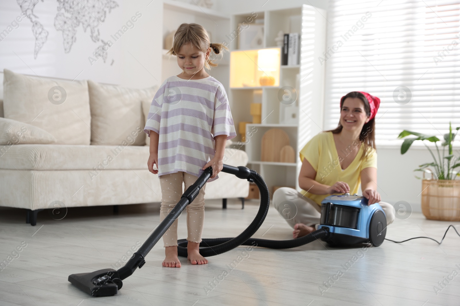 Photo of Little helper. Daughter and mother vacuuming together at home, selective focus