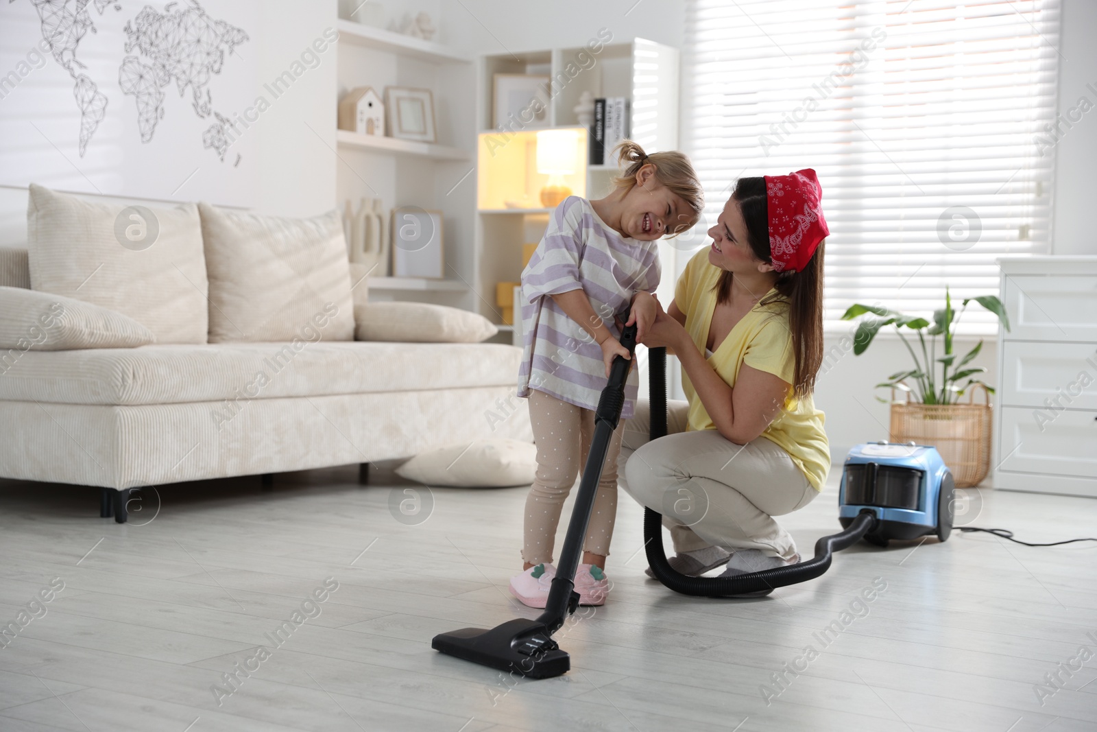 Photo of Little helper. Daughter and mother vacuuming together at home