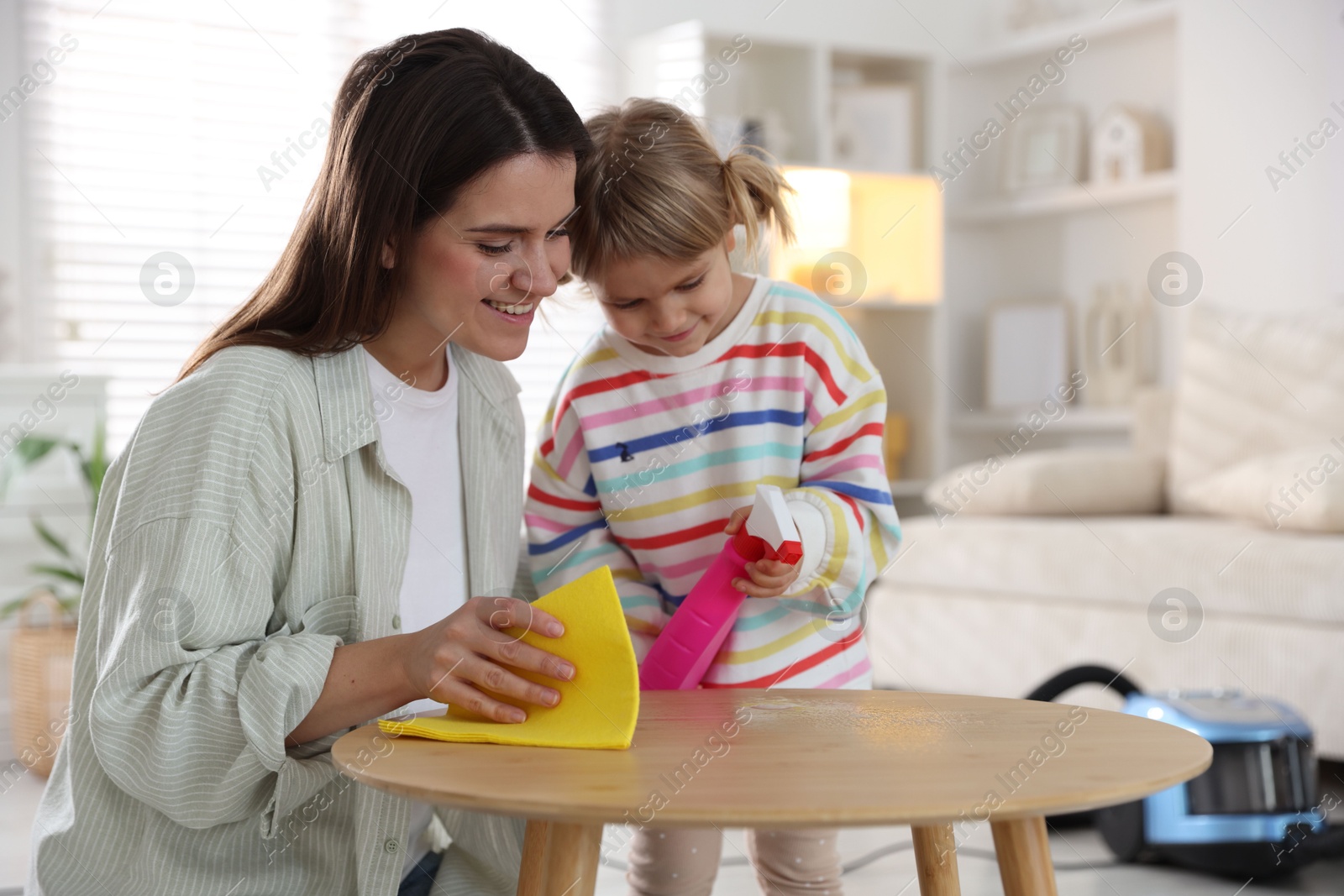 Photo of Cute little girl helping her mother wiping wooden table at home