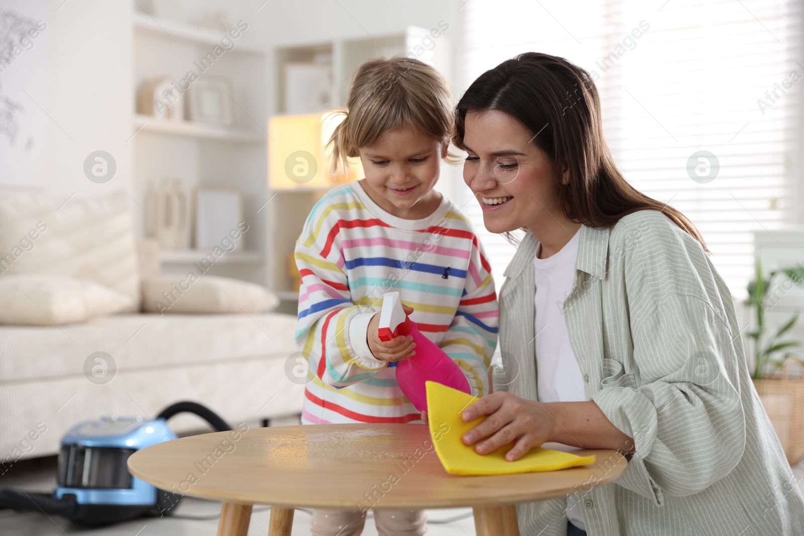 Photo of Cute little girl helping her mother wiping wooden table at home