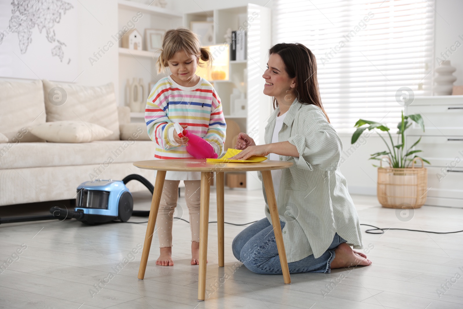 Photo of Cute little girl helping her mother wiping wooden table at home