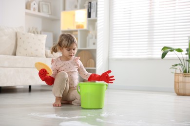 Photo of Little helper. Cute girl with sponge and bucket on floor at home