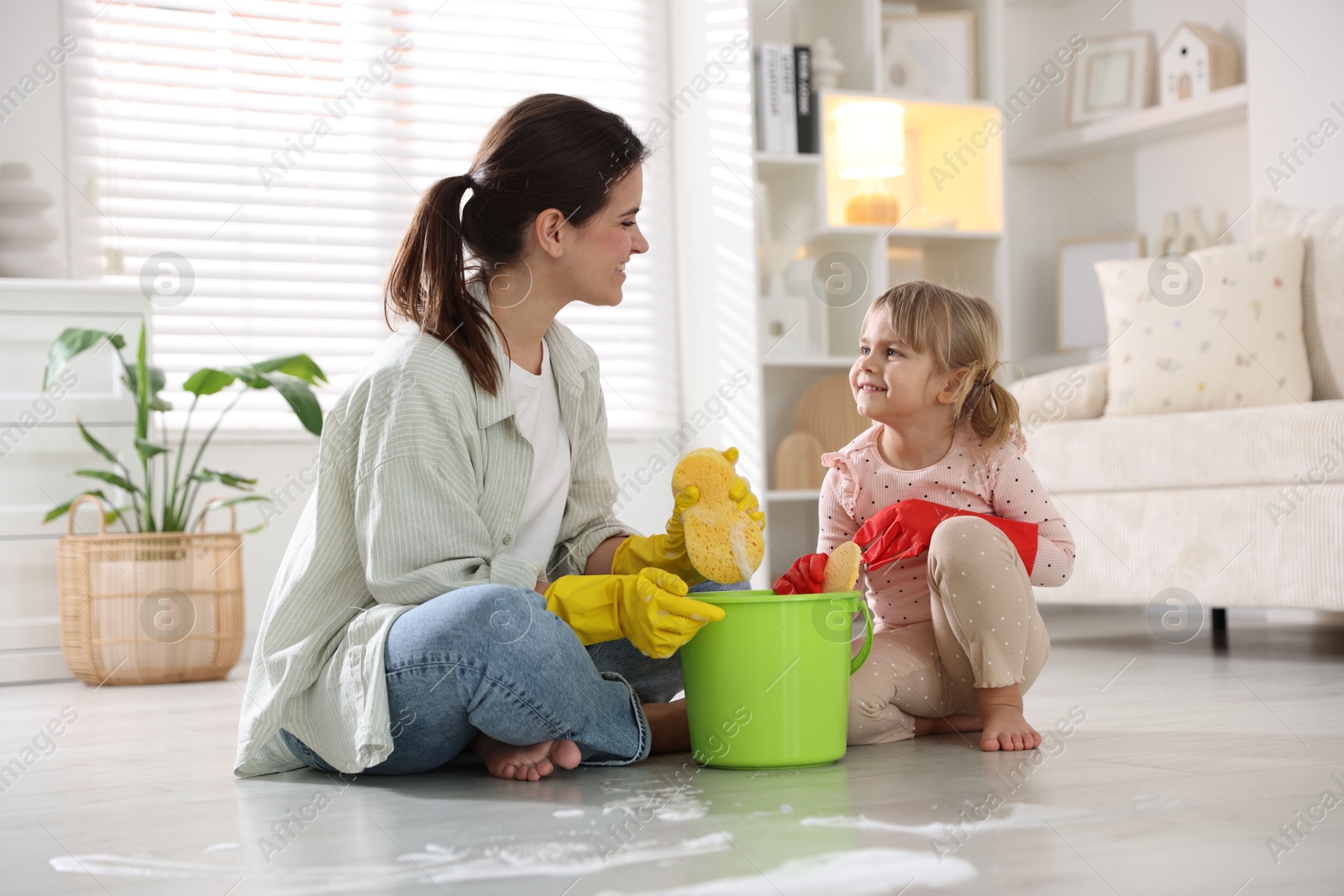 Photo of Cute little girl helping her mother cleaning floor at home