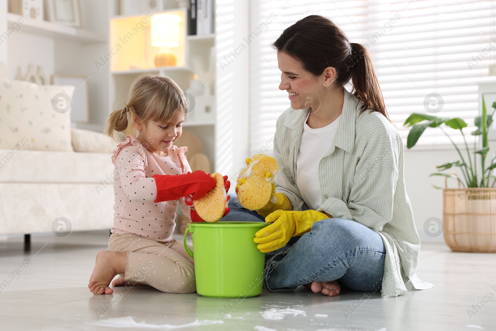 Photo of Cute little girl helping her mother cleaning floor at home