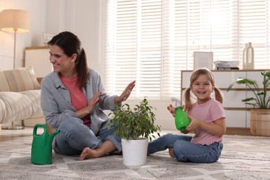 Photo of Cute little girl helping her mother watering houseplant at home