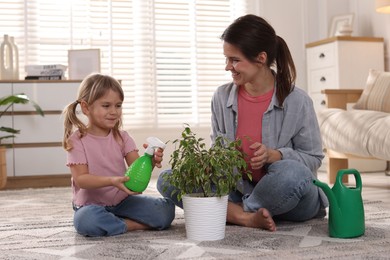 Photo of Cute little girl helping her mother watering houseplant at home