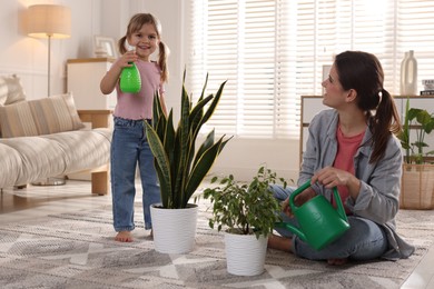 Cute little girl helping her mother watering houseplants at home