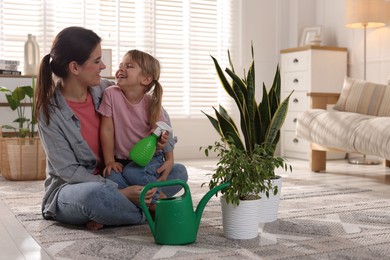 Photo of Little helper. Mother and her cute daughter with spray bottle near houseplants at home