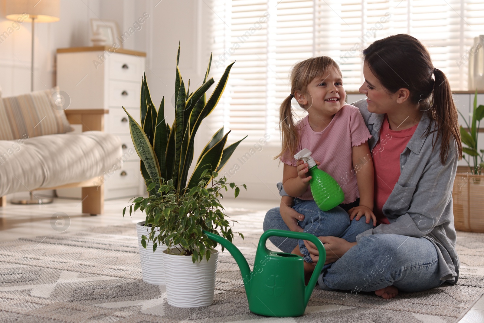 Photo of Little helper. Mother and her cute daughter with spray bottle near houseplants at home